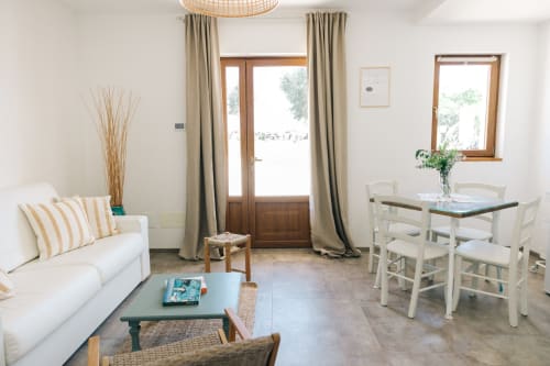 Bright garden-view apartment at Tenuta Fascianello with white sofa, dining table, and wood-framed doors opening to terrace.