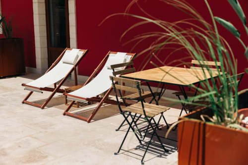 Sunny patio at Tenuta Fascianello with lounge chairs, dining table, potted plants, and vibrant red wall in Fasano.