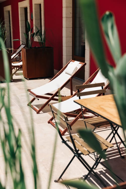 Sunny garden courtyard at Tenuta Fascianello Fasano with lounge chairs, potted plants, and red stone walls