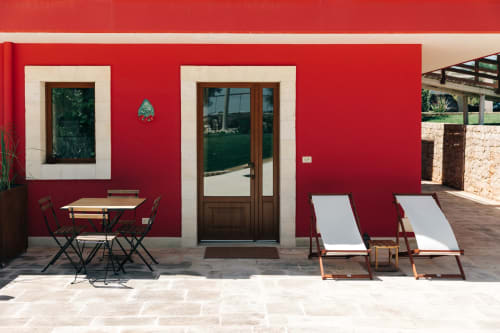 Red-walled patio at Tenuta Fascianello with table, deck chairs, and garden views in Fasano, Italy