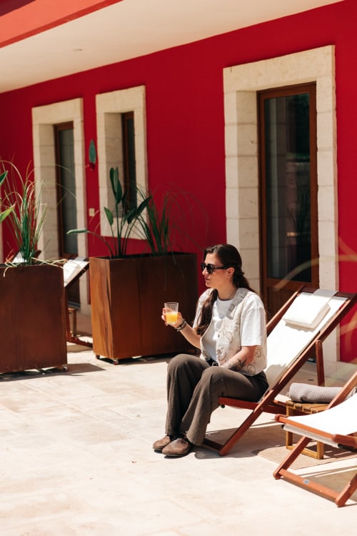Woman enjoying orange juice on lounge chair at Tenuta Fascianello's sunny garden patio with red walls