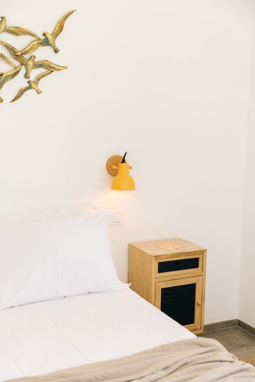 Camera minimalista a Tenuta Fascianello con biancheria bianca, comodino in legno, applique giallo e arte murale con rami dorati