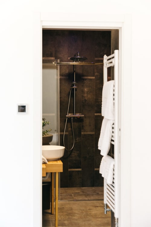 Bagno moderno a Tenuta Fascianello con doccia in piastrelle scure, soffione a pioggia, vanità in legno e scaldasalviette bianco riscaldato
