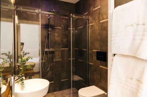 Bagno moderno con doccia in piastrelle marrone scuro, box doccia in vetro, lavabo bianco e toilette presso l'hotel Tenuta Fascianello a Fasano