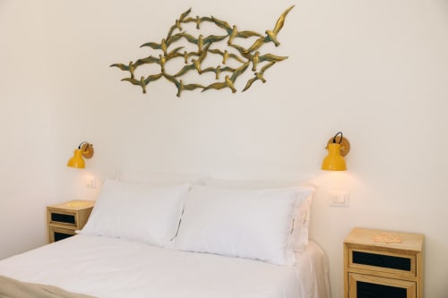 La camera Floral Sun di Tenuta Fascianello presenta un letto bianco con lampade a sospensione gialle e decorazioni artistiche di rami sulla parete