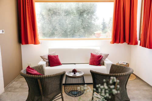 Luminosa zona soggiorno a Tenuta Fascianello a Fasano con divano color crema, sedie in vimini, tende rosse e vista sulla foresta