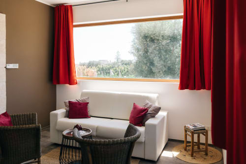 Luminosa camera d'albergo a Tenuta Fascianello con divano bianco, tende rosse e vista sulla campagna a Fasano, Italia