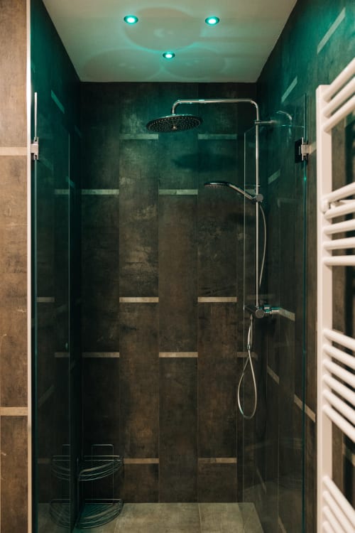Moderna doccia con piastrelle verde scuro, soffione pioggia e luci azzurre a soffitto nella Tenuta Fascianello