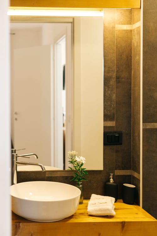 Bagno moderno a Tenuta Fascianello con lavabo bianco, specchio bronzeo, dettagli in piastrelle scure e piano in oro