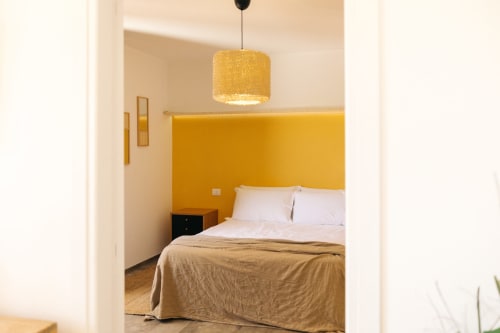 Camera da letto jungle all'Tenuta Fascianello con parete gialla, biancheria bianca e illuminazione a sospensione a Fasano