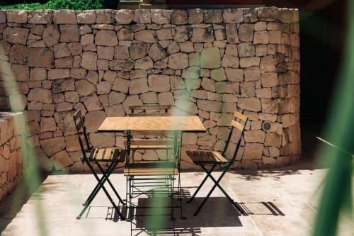 Tavolo in legno con sedie nere per cena all'aperto davanti al muro in pietra rustica di Tenuta Fascianello, Fasano