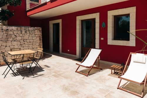 Terrazza soleggiata di Tenuta Fascianello con muri rossi, lettini, tavolo da pranzo e muro in pietra a Fasano