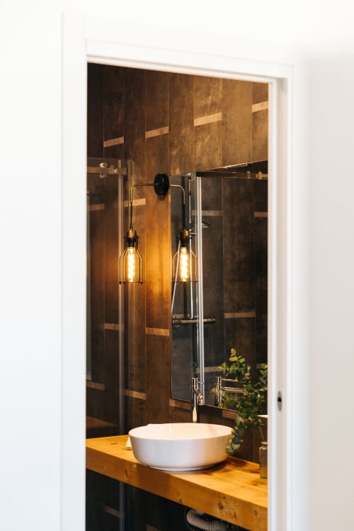 Bagno moderno a Tenuta Fascianello Fasano con lavabo a coppa bianco, pareti in piastrelle bronzee, lampade a sospensione e vista sul giardino.