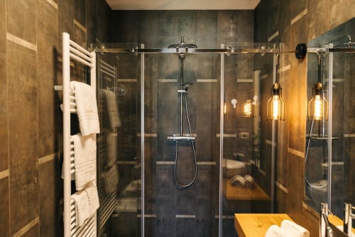 Moderna doccia con rivestimento in piastrelle scure, soffione a pioggia e lampade a sospensione presso Tenuta Fascianello