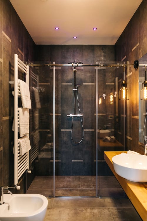 Bagno moderno a Tenuta Fascianello con doccia in piastrelle scure, lavabo bianco, dettagli dorati e scaldasalviette
