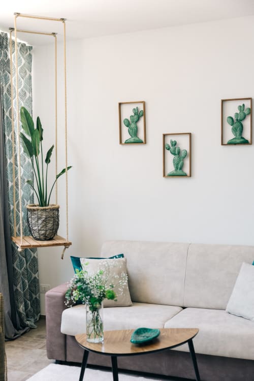 Luminosa sala al Tenuta Fascianello: divano beige, tavolo in legno, quadri di cactus, mensola con piante sospese e giardino