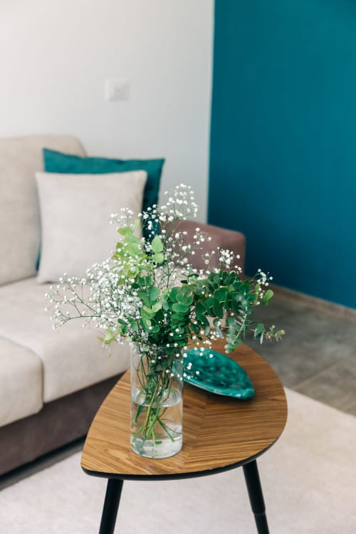 Elegante composizione floreale con gipsofila ed eucalipto in vaso di vetro su tavolo in legno accanto a divano color crema a Tenuta