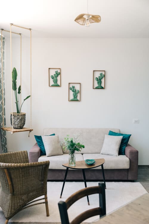 Luminoso soggiorno a Tenuta Fascianello con divano grigio, poltrona in vimini, mensola con piante sospese e arte murale di cactus, Fasano Italia