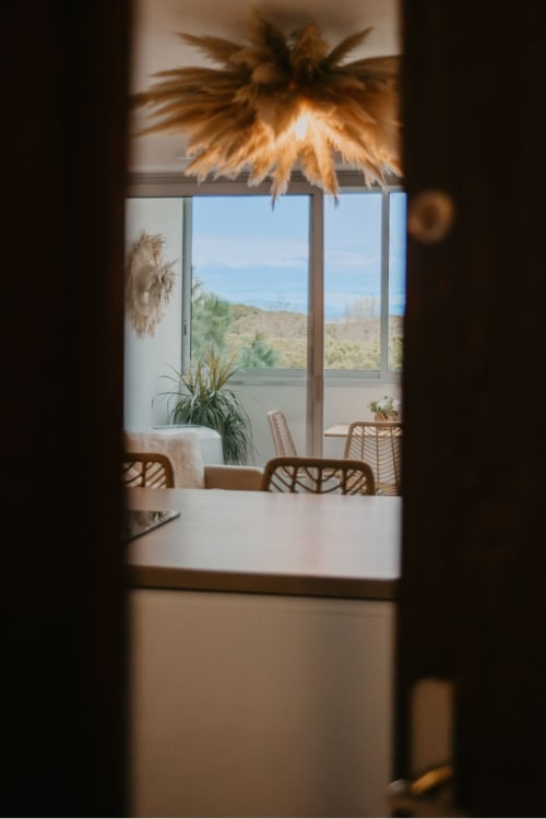 Vue de la chambre d'hôtes Sable & Pampas par l'encadrement de la porte, décoration de palmiers et paysage désertique
