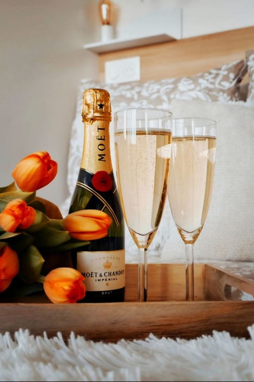 Célébration au champagne à Sable & Pampas : bouteille Moët & Chandon avec flûtes et tulipes orange sur plateau en bois.