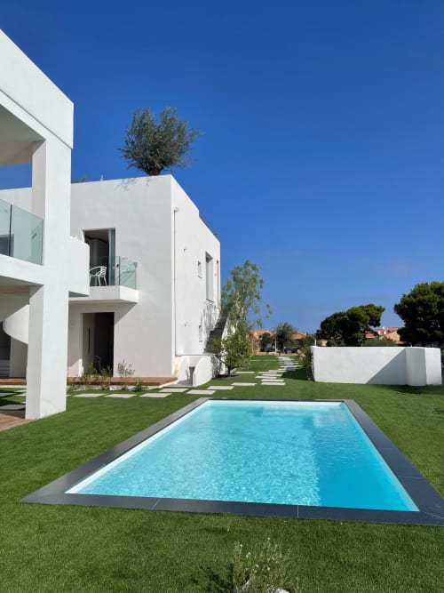 Villa bianca moderna al Like at Home Palau con piscina turchese, prato verde e paesaggio mediterraneo in Sardegna