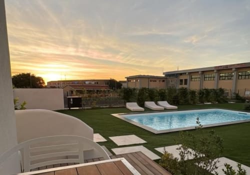 Area piscina esterna Like at Home Palau con lettini, prato curato e vista sul tramonto in Sardegna