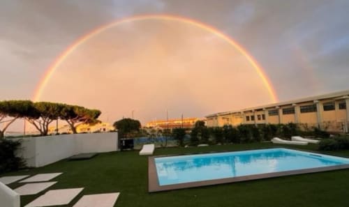 Doppio arcobaleno sopra la piscina Like at Home Palau al tramonto, prato verde e architettura costiera italiana