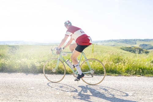 Cyclist in red helmet riding on gravel road through Tuscan countryside near Buonconvento, Siena, Italy