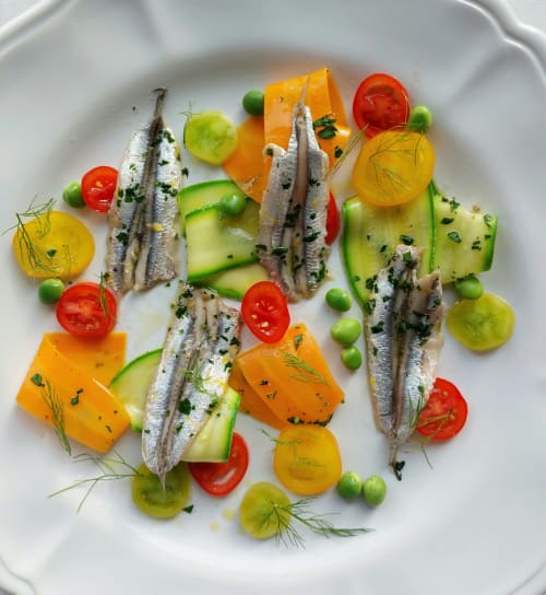 Elegante piccolo pesce in piatto con verdure colorate ed erbe aromatiche presso il ristorante Aura Relais a Numana