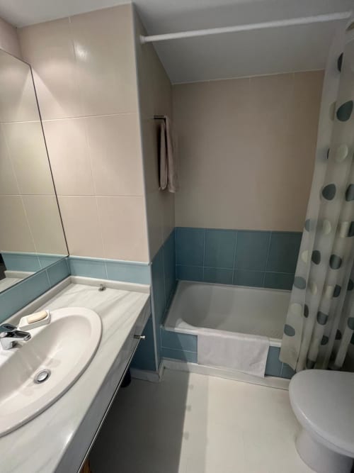 Moderno baño del apartamento Sant Jordi con azulejos azul y beige, bañera, lavabo, inodoro y cortina de ducha