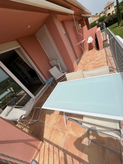 Amplia terraza con tumbonas, edificio rojo y vistas al campo de golf en el apartamento Sant Jordi cerca de la playa
