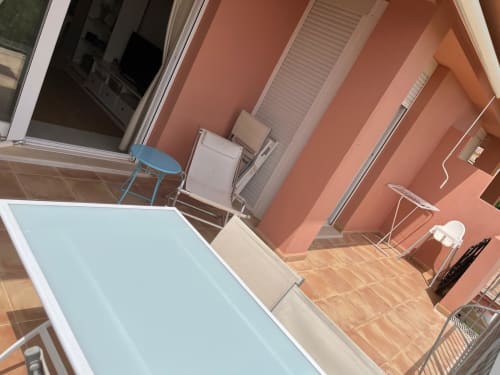 Amplia terraza de apartamento en Sant Jordi con tumbonas, zona de comedor y paredes color coral con vistas al jardín