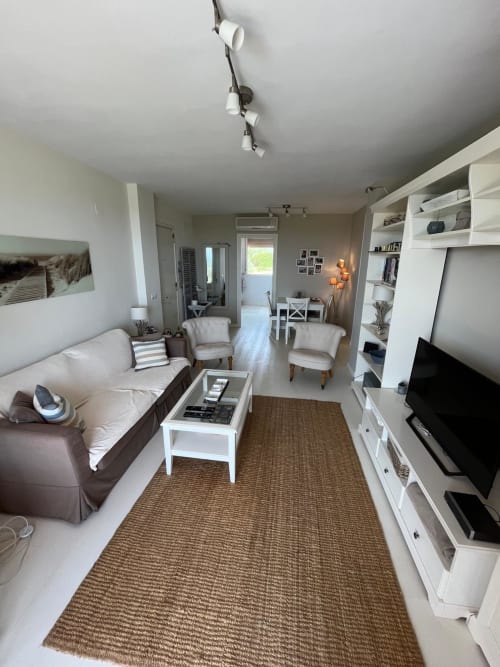 Salón moderno del apartamento Sant Jordi con sofá, televisión, estantería blanca y vistas al jardín cerca de la playa