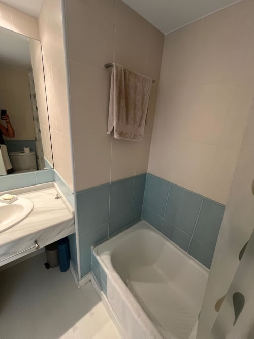 Cuarto de baño moderno con bañera, azulejos azules, lavabo, espejo y toallero en apartamento Sant Jordi