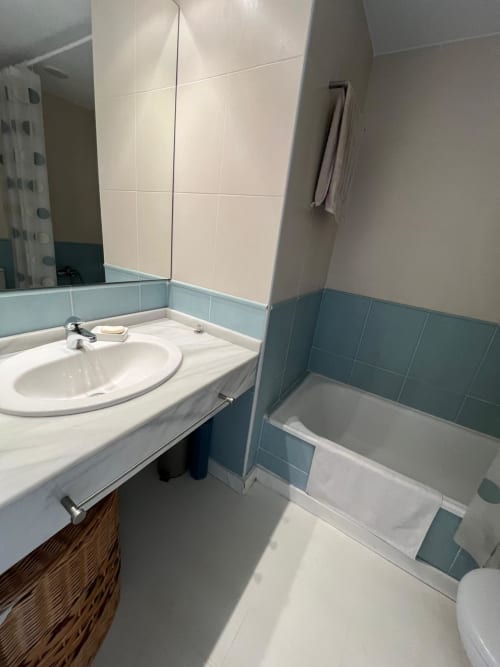 Baño moderno con lavabo, bañera, azulejos en tonos verde azulado y crema, espejo y toallero en el apartamento Sant Jordi