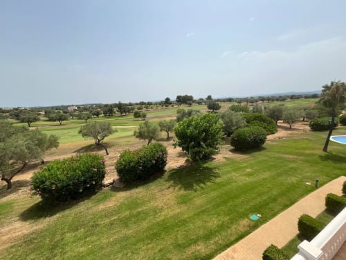Vista al campo de golf desde el jardín del apartamento en Sant Jordi con céspedes bien cuidados, olivos y terraza de piscina