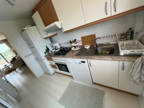 Cocina moderna en apartamento Sant Jordi con gabinetes blancos, electrodomésticos de acero inoxidable y encimeras de granito cerca de la playa
