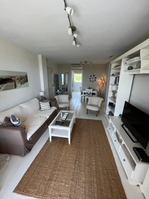 Salón moderno con vistas al golf, almacenamiento blanco, sofá marrón y acceso a terraza cerca de playa Sant Jordi