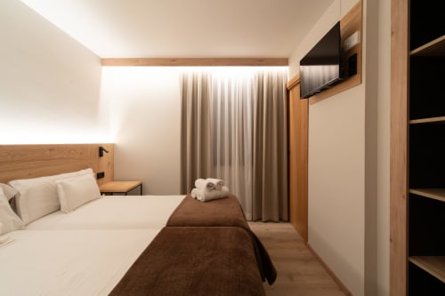Dormitorio doble moderno en Hotel Bruna en Esterri D'Àneu con toques de madera, TV pantalla plana y ropa de cama neutra