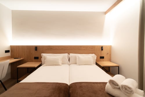 Moderno dormitorio doble en Hotel Bruna con cabecero de madera, ropa de cama crema, calefacción radiante y comodidades contemporáneas