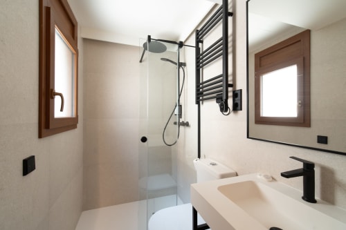 Baño moderno en Hotel Bruna con ducha lluvia, accesorios negros y toallero calefactable