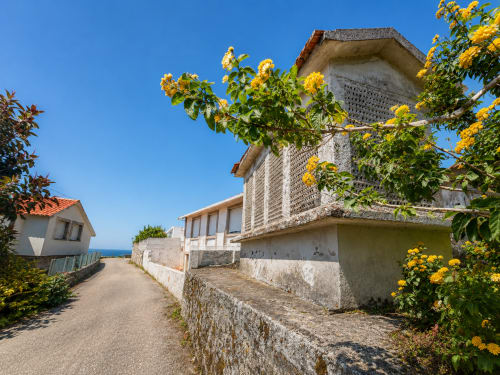 Hotel Holibai en Baiona con flores amarillas, edificios de piedra y vistas al mar bajo cielo azul