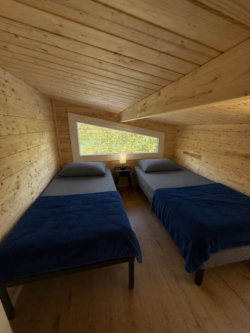 Chambre douillette du lodge en bois avec deux lits jumeaux et couvertures bleues aux Cabanes et lodges du Belvédère, Serrières-sur-Ain