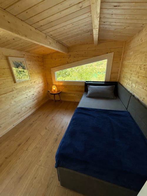 Chambre de lodge moderne en bois aux Cabanes du Belvédère avec lit, grande fenêtre donnant sur la nature, poutres et parquet en bois