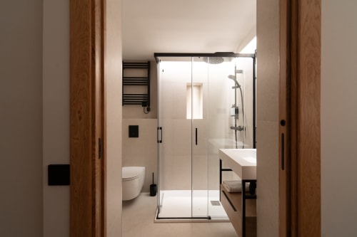 Baño moderno del Hotel Bruna con cabina de ducha de cristal, lavabo blanco, inodoro y toallero climatizado en Esterri d'Àneu