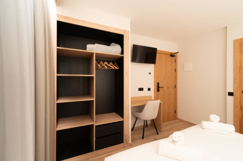 Habitación moderna del Hotel Bruna con armario de madera, escritorio, televisor y ropa de cama blanca en Esterri D'Àneu