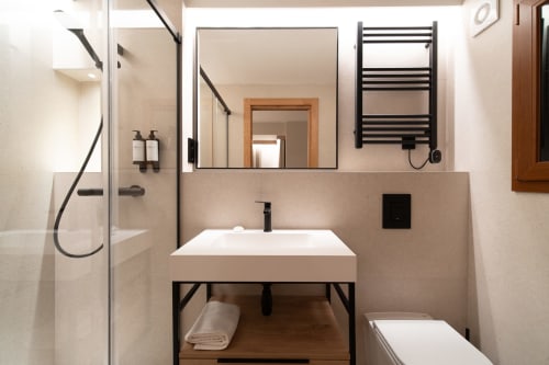 Baño moderno en Hotel Bruna con lavabo blanco, accesorios negros, toallero calefactor y ducha a ras de suelo en Esterri D'Àneu