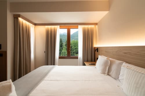 Moderna habitación doble en Hotel Bruna de Esterri D'Àneu con vistas a las montañas, cabecero de madera y puertas de terraza con cortinas