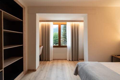 Moderna habitación doble en Hotel Bruna con suelos de madera, cama, estanterías y puertas de cristal con vistas a las montañas de Esterri