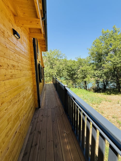 Terrasse en bois avec garde-corps noir surplombant le paysage forestier du lac aux Cabanes et lodges du Belvédère